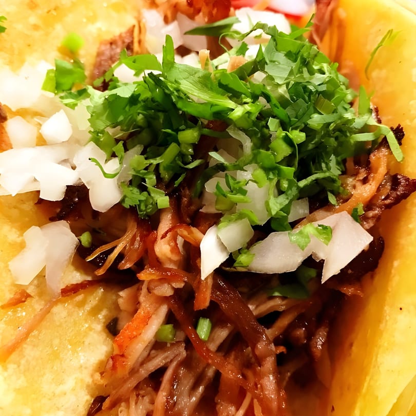 Close-up of a Sol Azteca Mexican taco filled with shredded meat, diced onions, and cilantro.