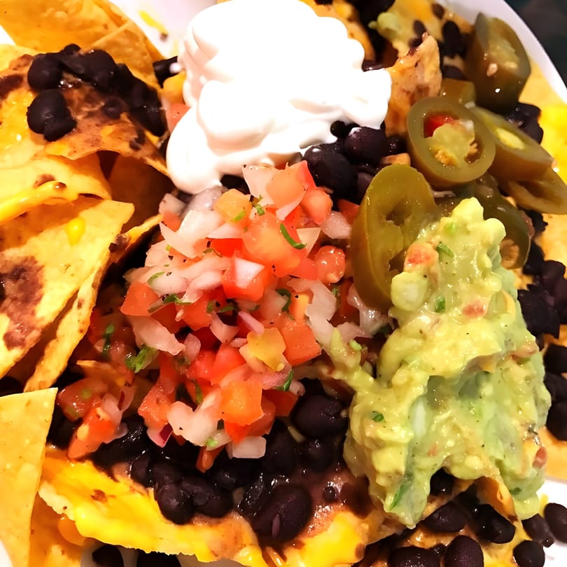 Close-up of Sol Azteca nachos with black beans, melted cheese, pico de gallo, guacamole, and sour cream.